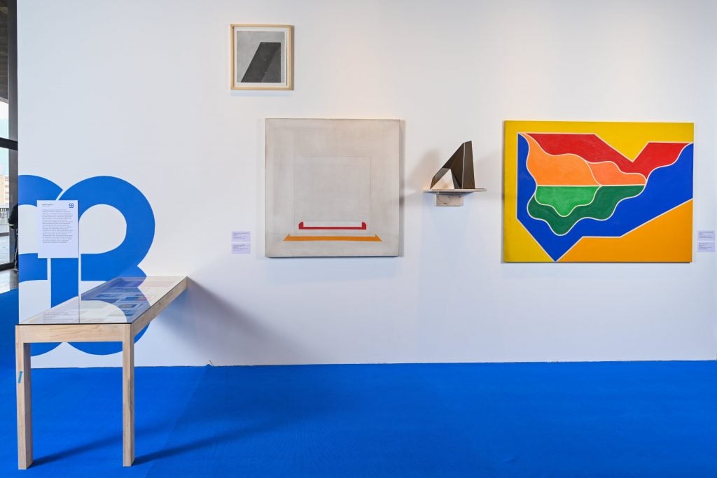 a gallery has bright blue caprteign and minimal geometric paintings on the wall