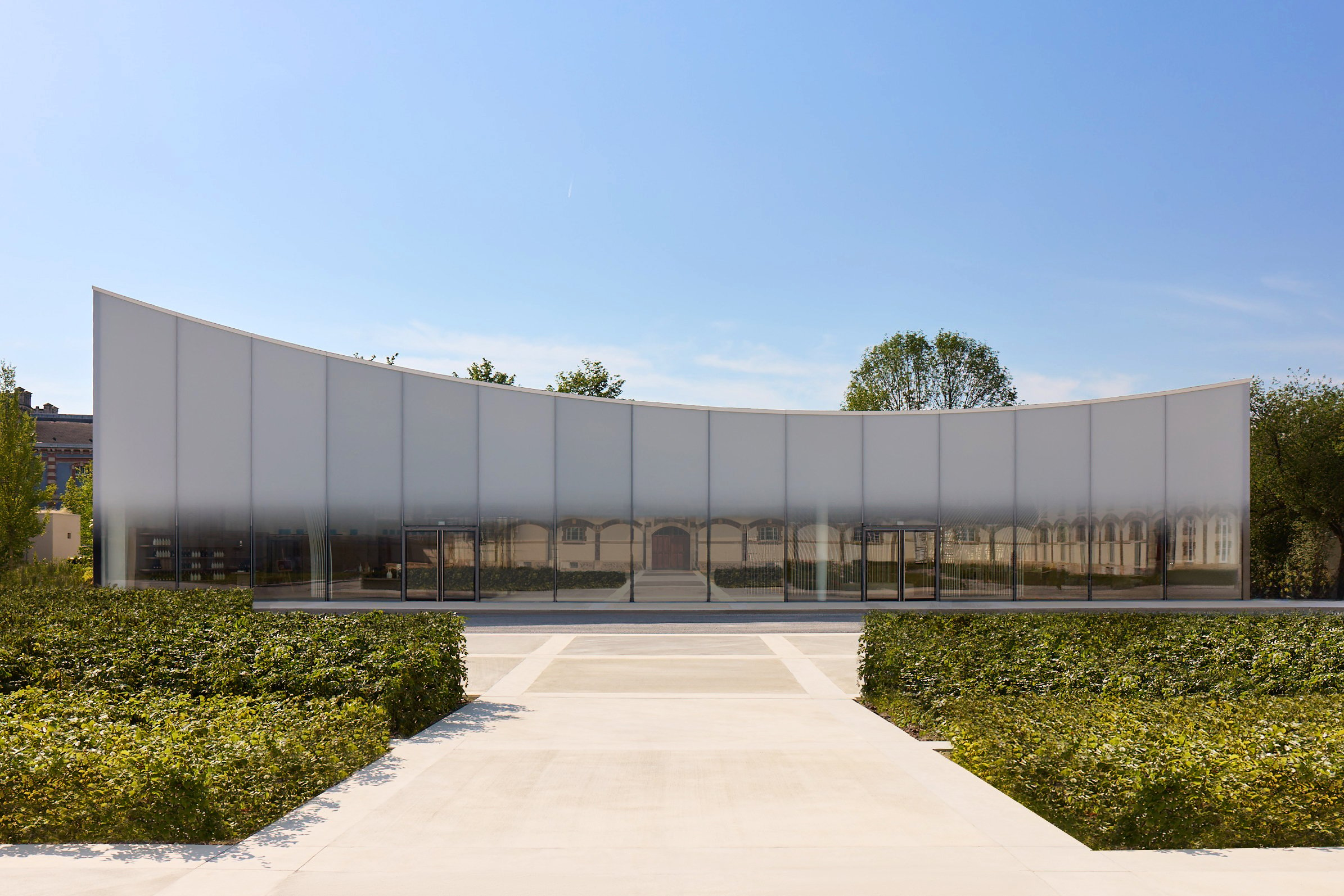 an external view of the glass facade of the Nicolas Ruinart Pavillion, set within a courtyard and blue open sky above