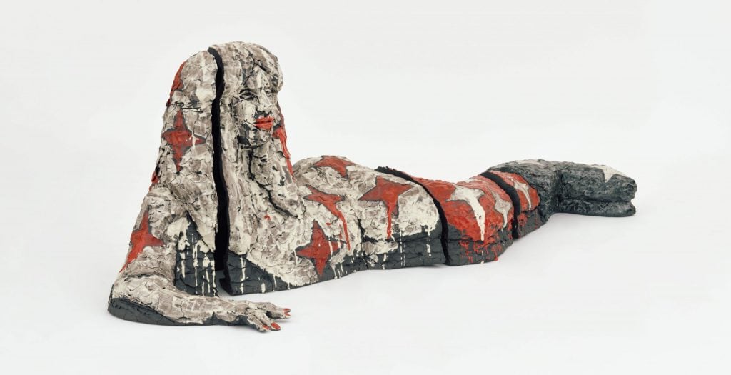 a sculpture in white, black, and red of a female figure lying on her side