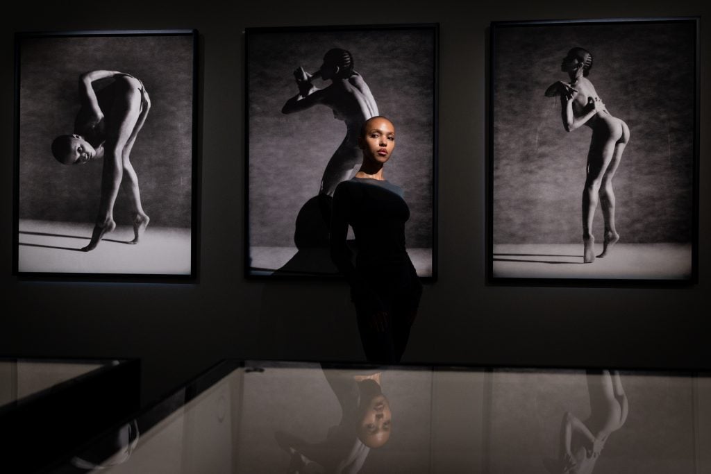 a woman stands in a dark room in front of three large black and white photos of herself dancing