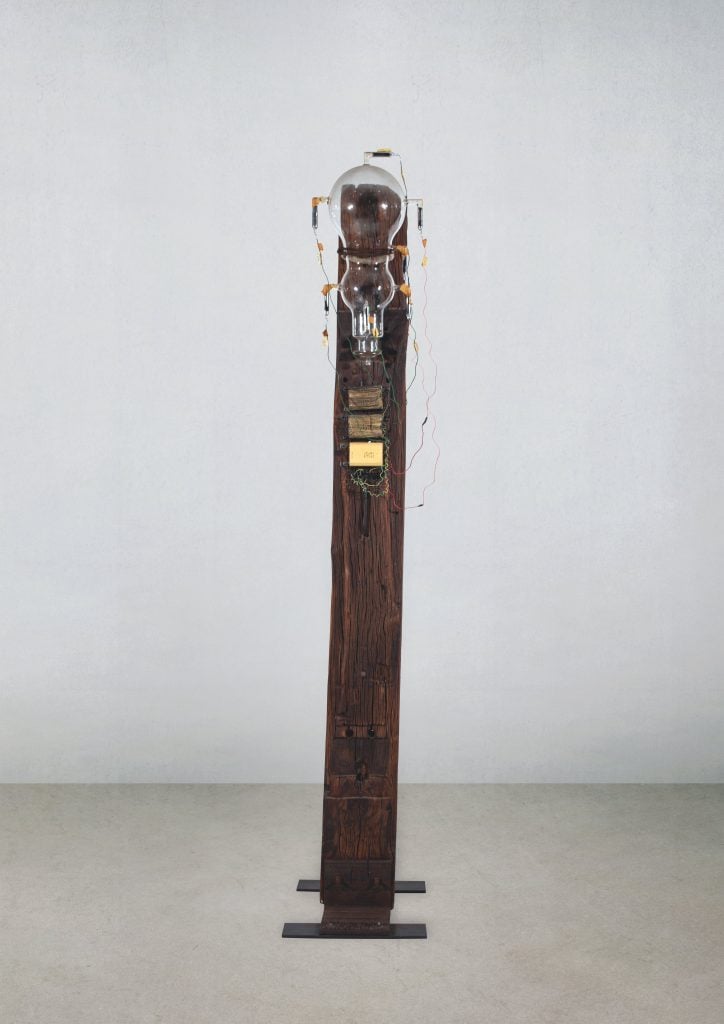 A vertical found object sculpture with some sort of glass lightbulb object at the top y the Greek artist Takis, featured in the inaugural exhibition at L'Appartement.