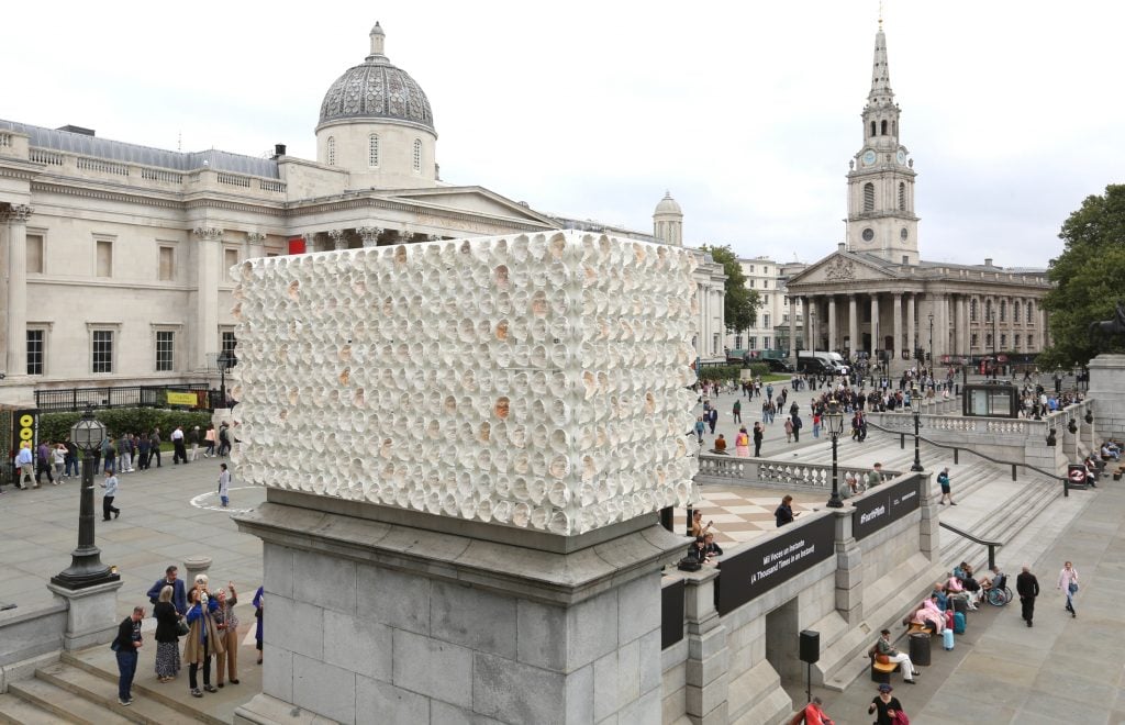 a large urban square lined with classical buildings. In the center in the foreground of the photo is a rectangular plinth carrying another rectangular structure made up of small pieces of ceramic