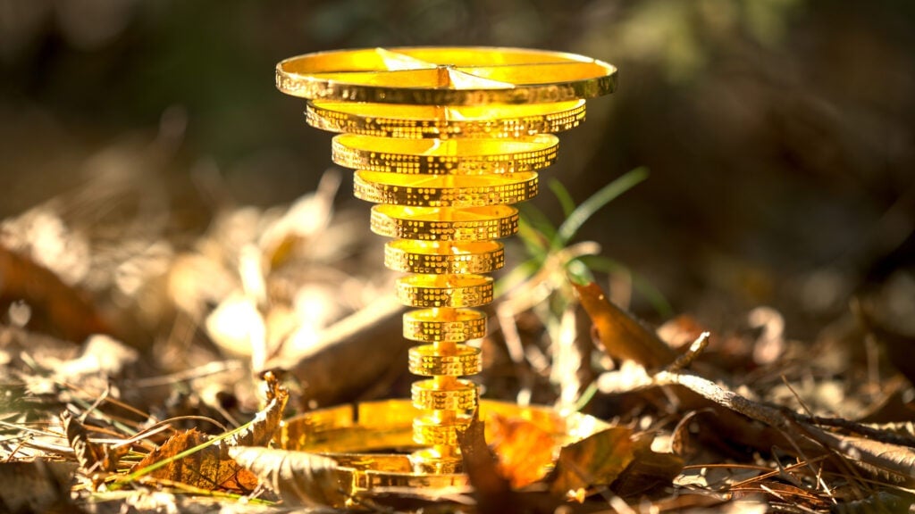 a golden statuette in the design of a tornado stands amongst dry leaves in a close up shot