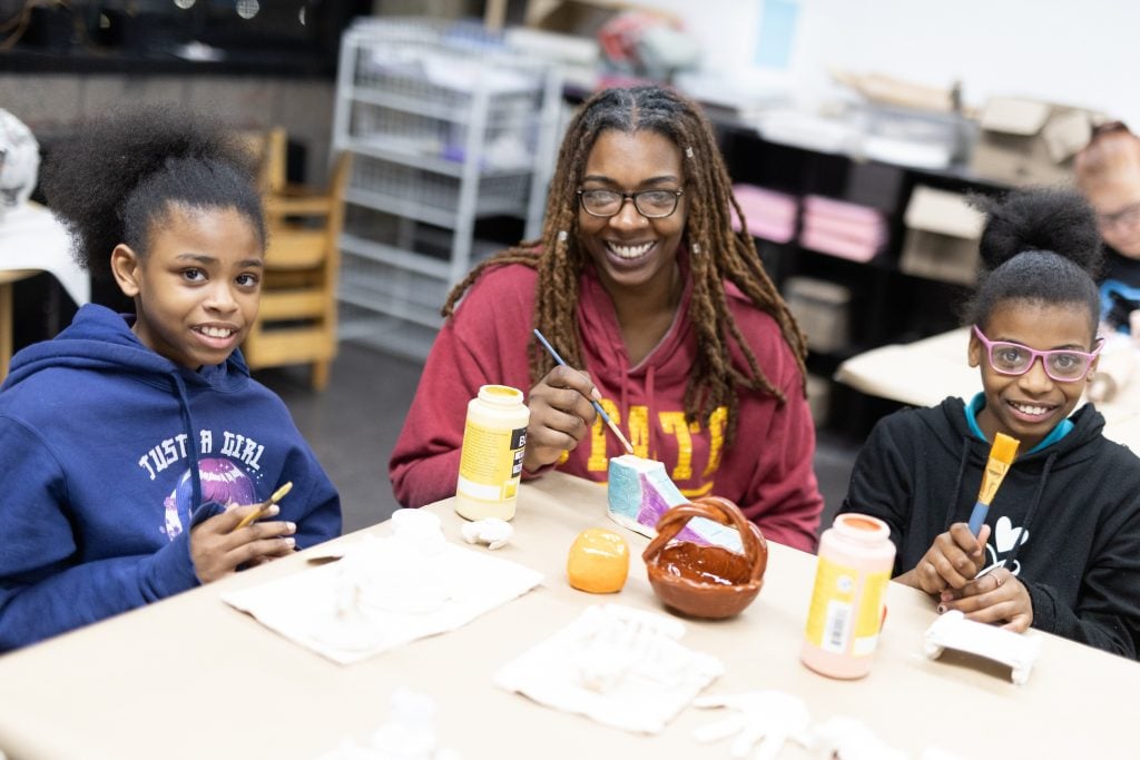 Two girls and a young woman work on ceramics in an art workshop