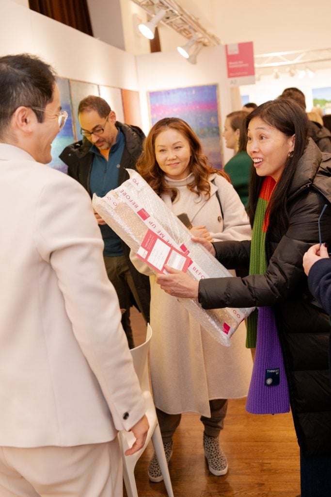 A small group of visitors to Affordable Art Fair NYC chatting and looking at a fair map.