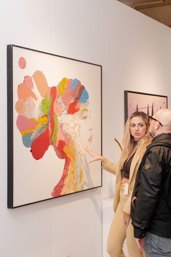 Two visitors to Affordable Art Fair NYC look at an abstract painting installed in a booth.