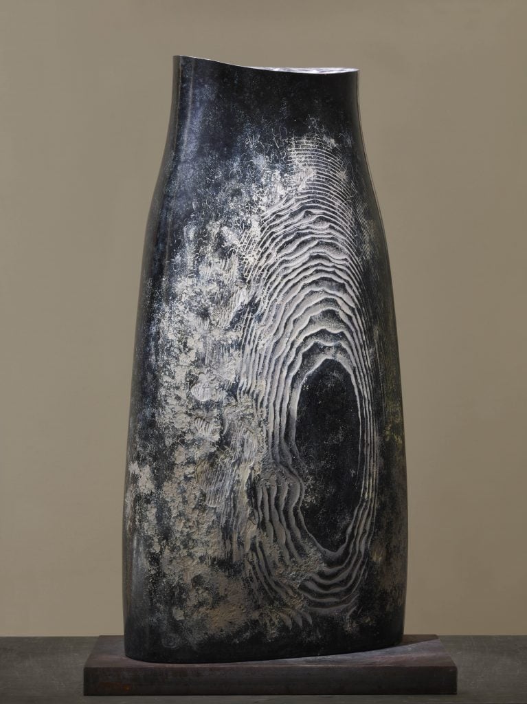 A stone sculpture that appears like a vessel, dark in color but etched on the front revealing paler material beneath, the etching looks like tree rings or a fingerprint, included at the inaugural exhibition at L'Appartement, Geneva.