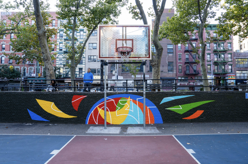 A photograph of a colorful mural painted on the wall lining an outdoor basketball court.