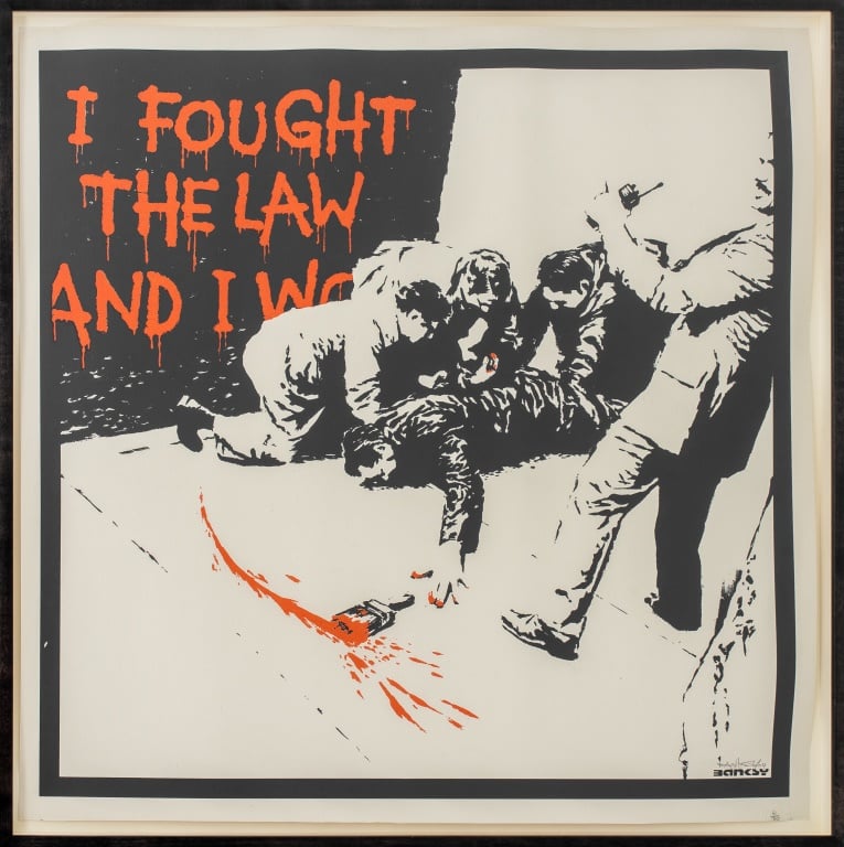 A black-and-white silkscreen image by banksy showing three suited men pushing down a man wearing black, and another standing with a walkie talkie. Painted on the wall behind in orange is the text 