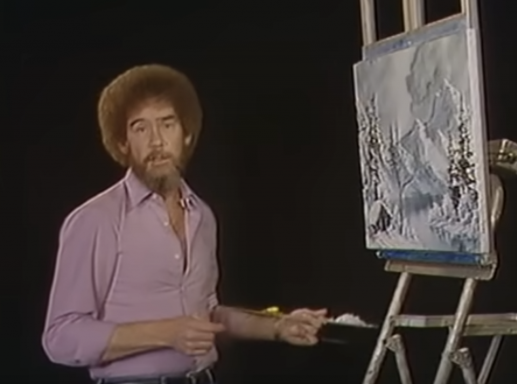 A photograph of Bob Ross standing before an easle, looking at the camera.