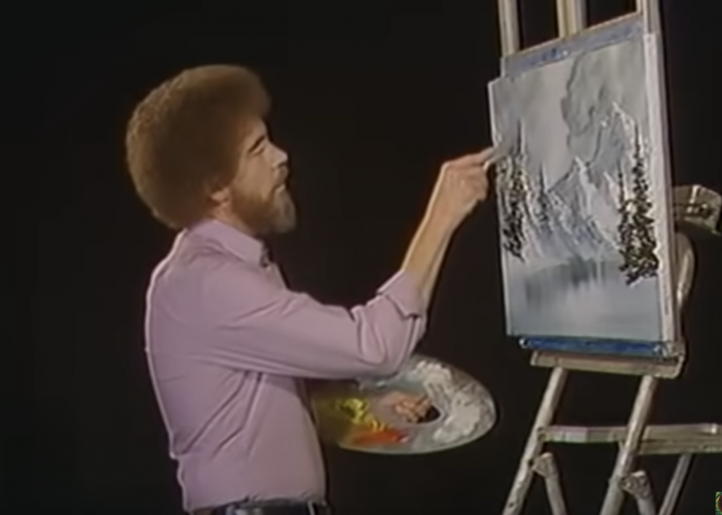 A photograph of Bob Ross painting a grayscale mountain scene