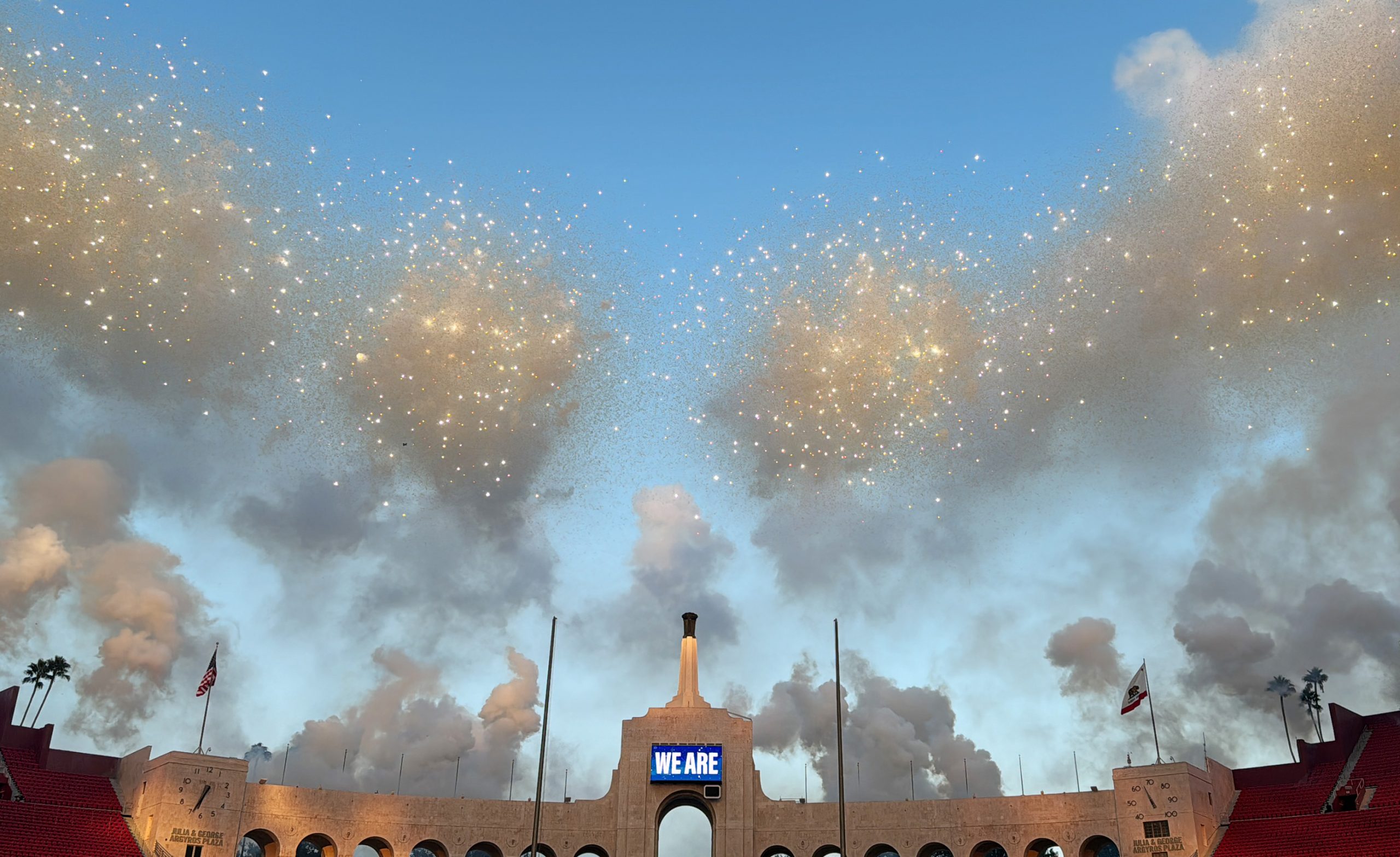 A cloud of fireworks against a structure with a screen that reads "WE ARE"