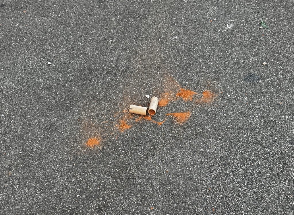 A paper tube spilling orange powder on a road surface