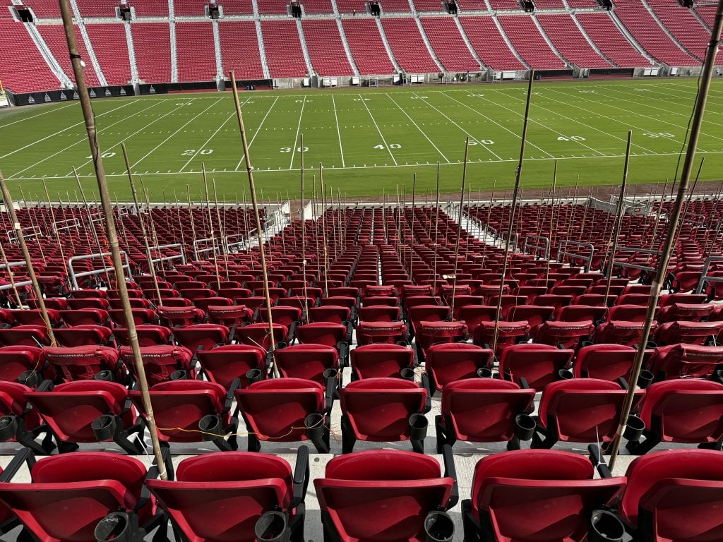 A section of a stadium's bleachers showing red chairs with bamboo poles attached to their side