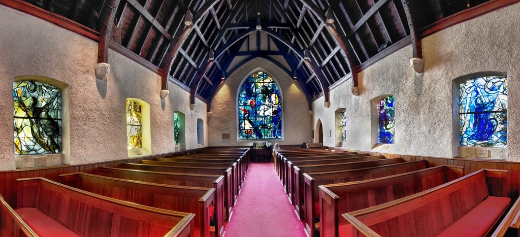 View of a church with a large stained-glass window behind the altar and eight other stained-glass windows lining the sides