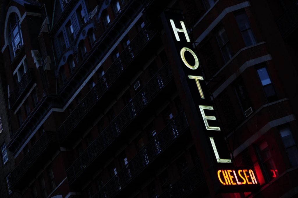 A photo of the exterior of the Chelsea Hotel at night, with its neon sign reading 