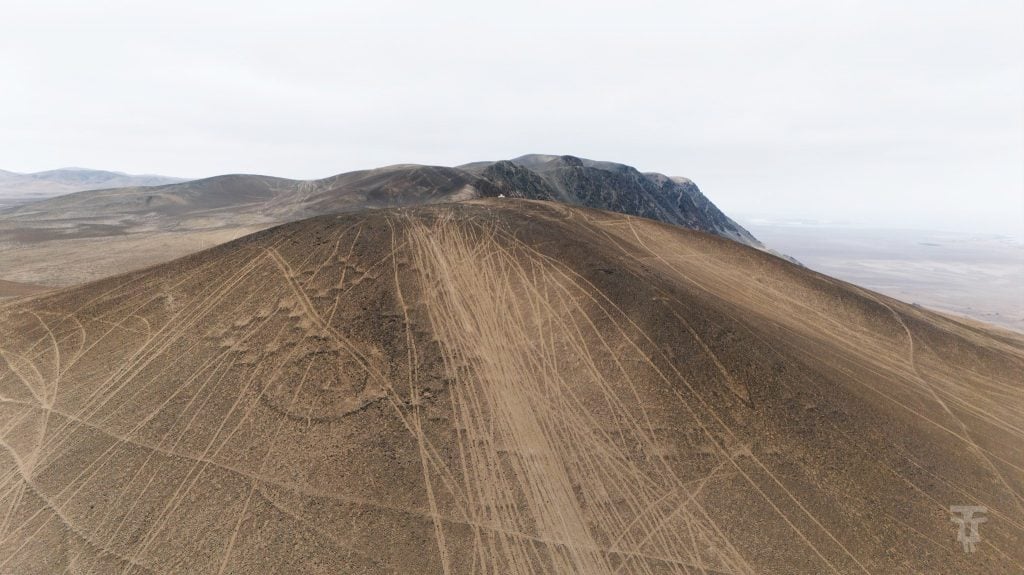 Aerial view of vehicle tracks crisscrossing ancient geoglyphs in a desert landscape