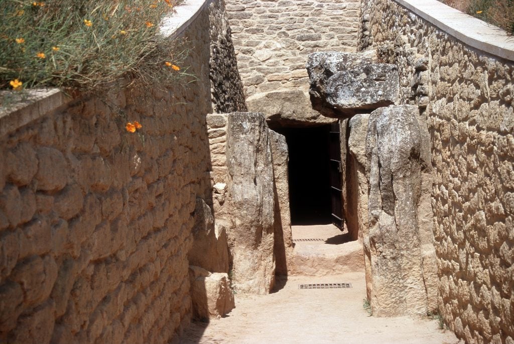 A sandy path leading to the entrance of a tomb, framed by large rocks.