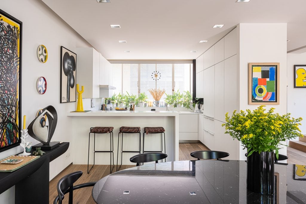 A large black dining table in the foreground and a sunlit kitchen in the background