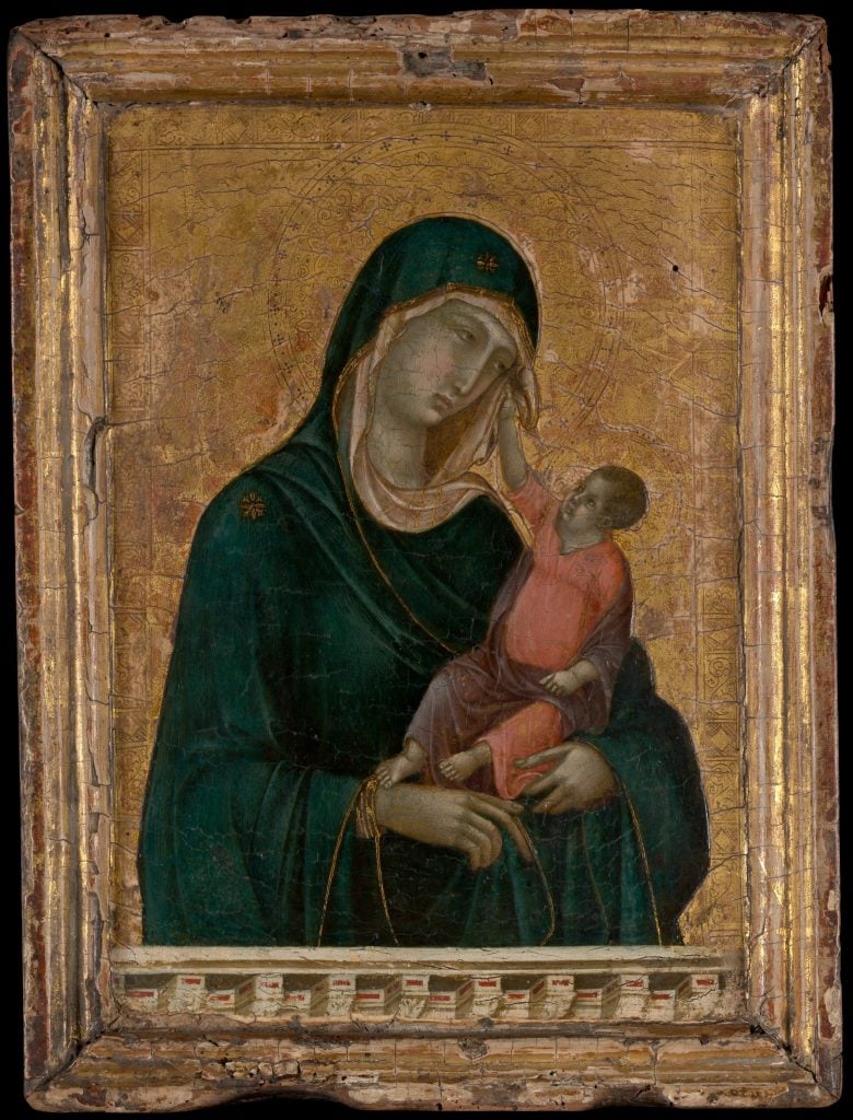 An image of an early Renaissance paiting by Duccio di Buoninsegna depicting the Virgin Mary in blue holding baby Jesus, who reaches up towards her while wearing pink, all on a solid gold background in a gold frame.