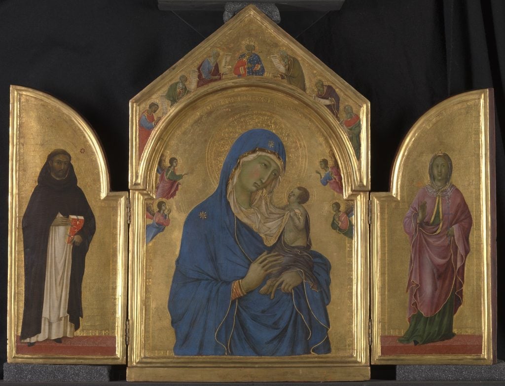 A photo of a tryptych depicting the Virgin Mary and Christ Center, flanked by a single saint on either side, all painted on gold backgrounds with arched shapes on the sides and a pointed top over the center.