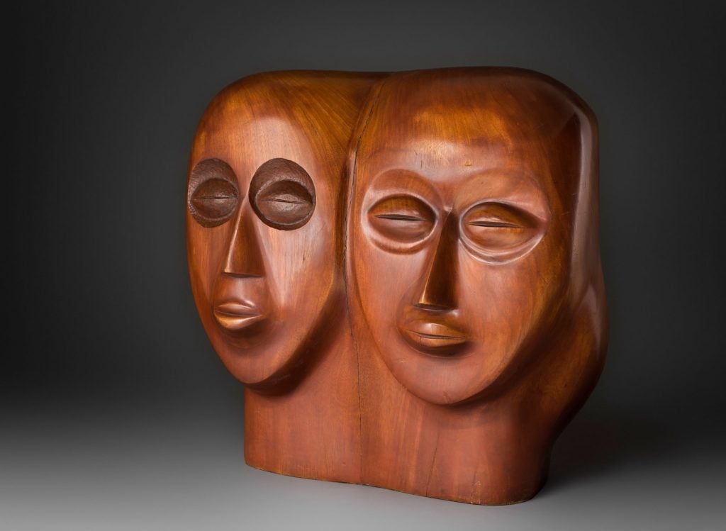 A wooden sculpture of two heads fused at the ear