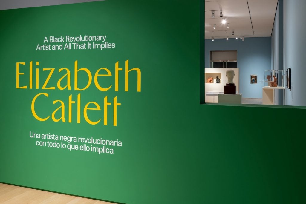 A gallery wall painted green with the title "“Elizabeth Catlett: A Black Revolutionary Artist and All That It Implies”