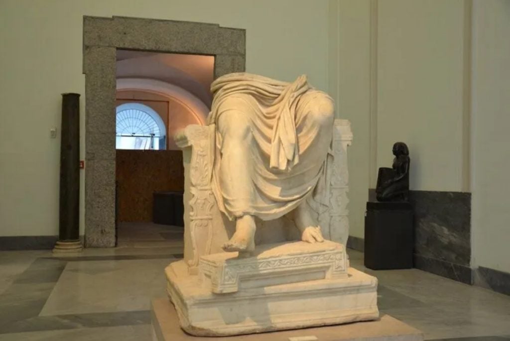 A photograph of a marble sculpture depicting Jupiter only from the waist down within the white walls of a museum in Naples.