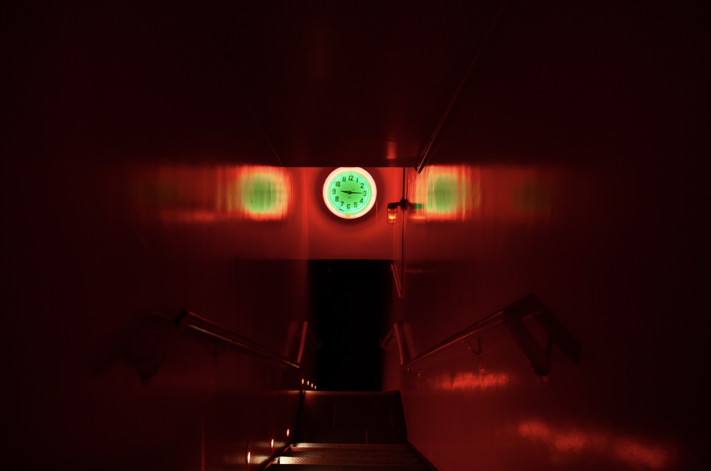 A photograph of a dark red entrance to a club, with a green-lit clock over top.