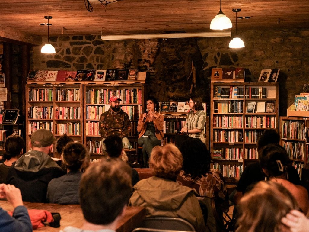 A photograph of three speakers giving a panel discussion in a book store before a seated crowd.