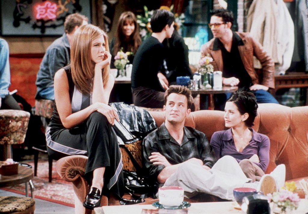 On the cafe set of the TV show Friends, two women and a man are sitting on a couch