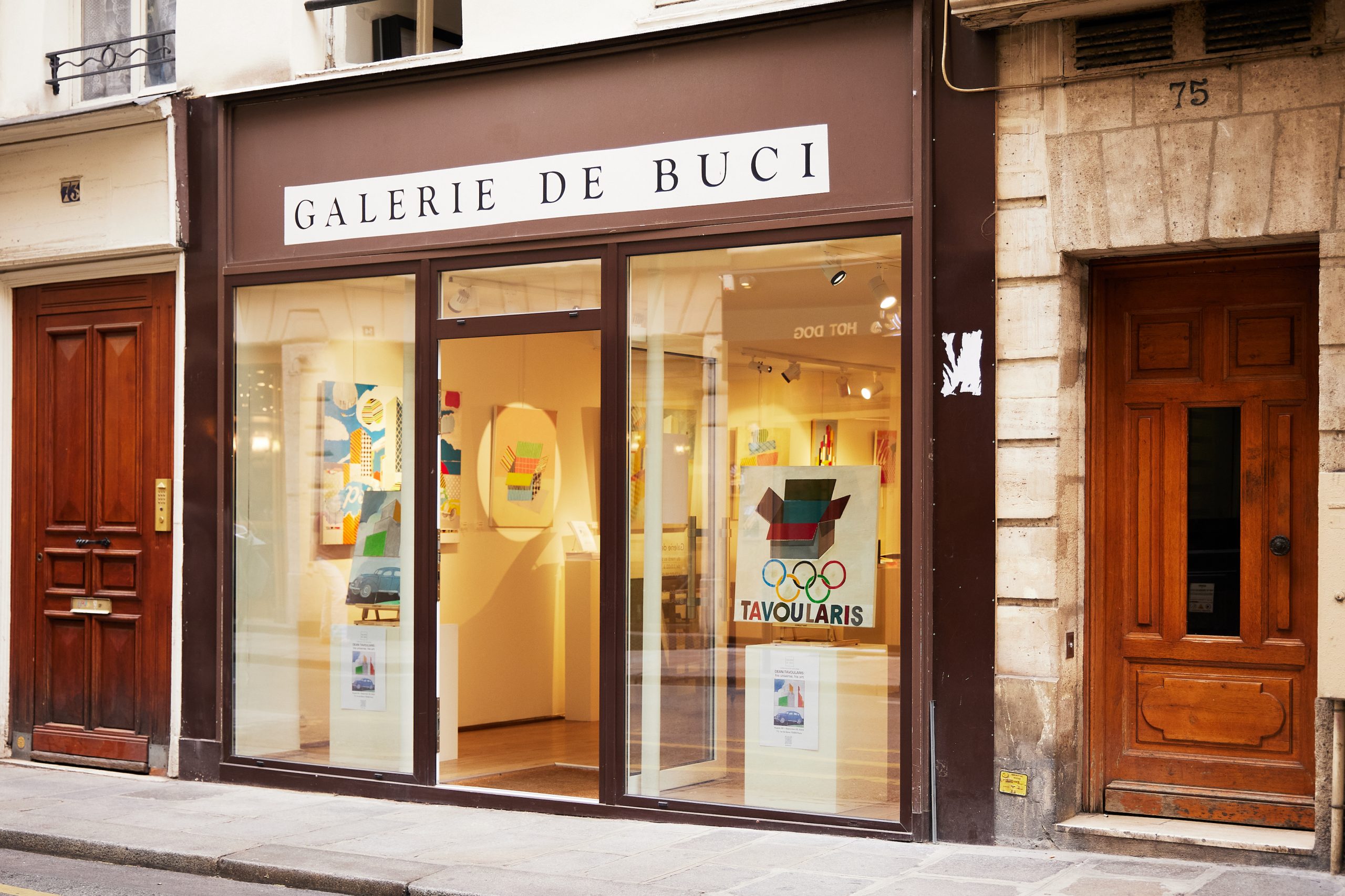 An exterior photo of Galerie De Buci in Paris showing artwork installed in the two front glass window walls.