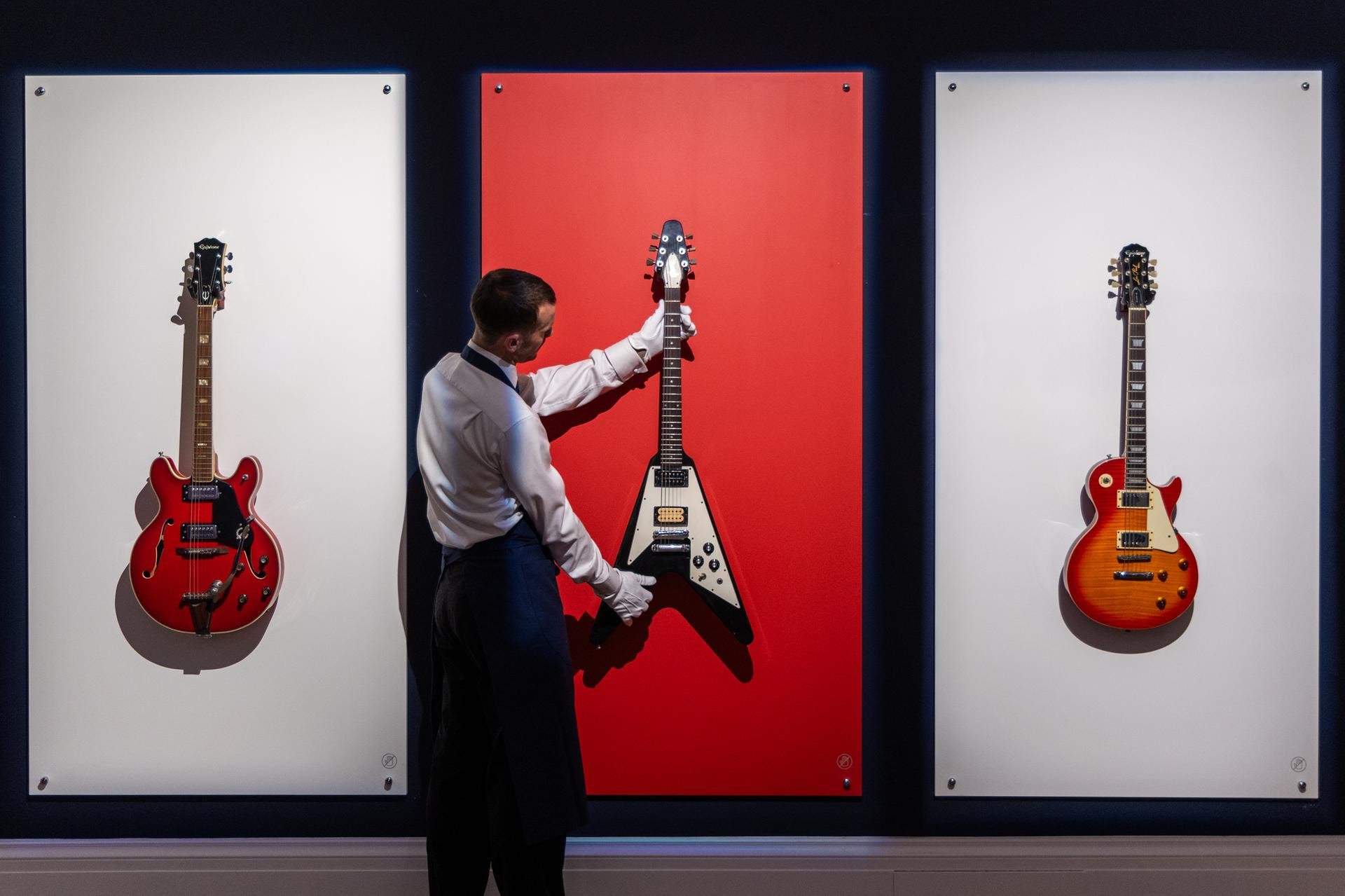 row of three guitars on a wall with a man checking the alignment