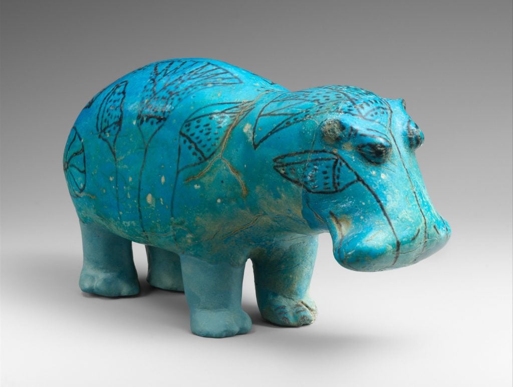 a small turquoise blue figurine in the shape of a hippopotamus against a grey background