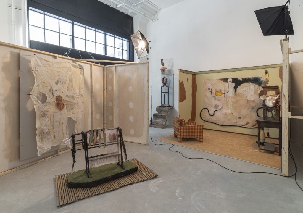 Installation view of "Amy Bravo: TransmogrificationNow!" showing two partially constructed rooms with paintings and sculptures by Amy Bravo.