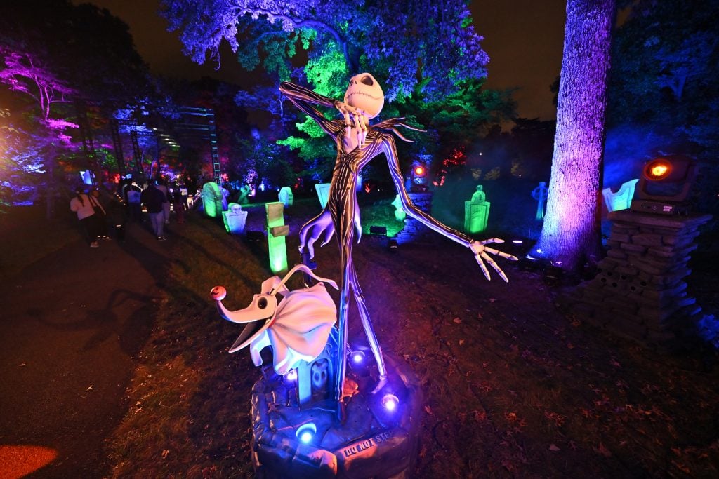 A photograph of a sculpture depicting Jack Skellington from The Nightmare Before Christmas amongst an installation of illuminated gravestones in a forest.