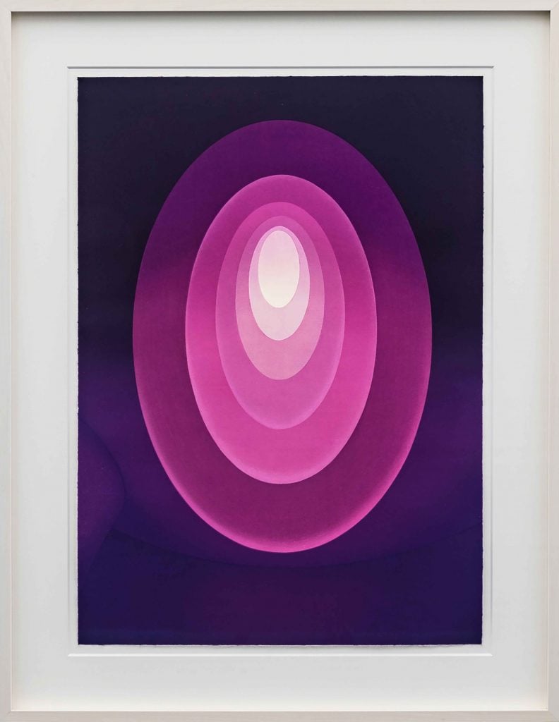 A photograph of a woodblock print of an abstract, geometric artwork of concentric magenta ovals with a white center, hanging on a white wall.