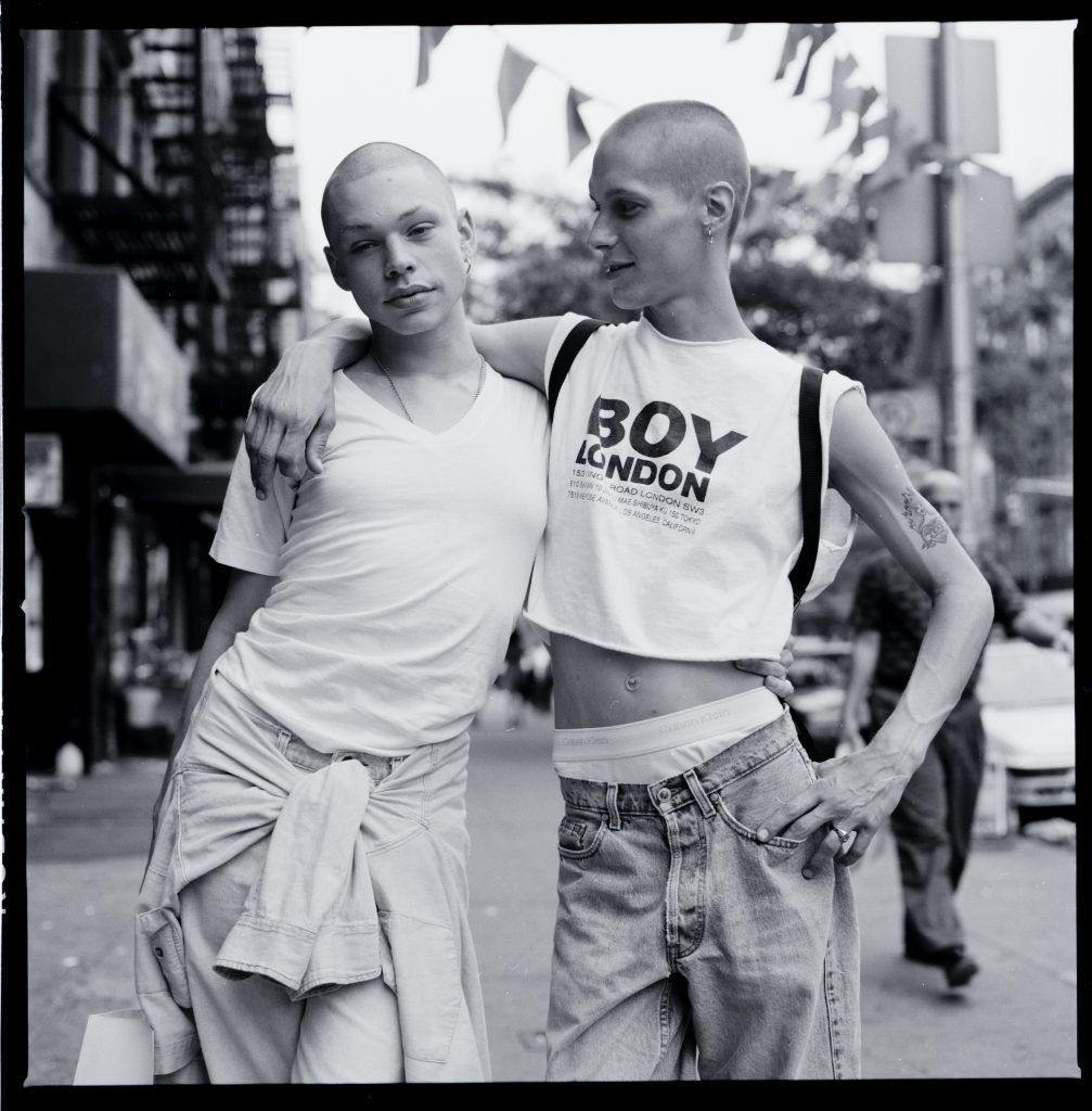 A black and white portrait of two people wearing street clothes and leaning on one another.