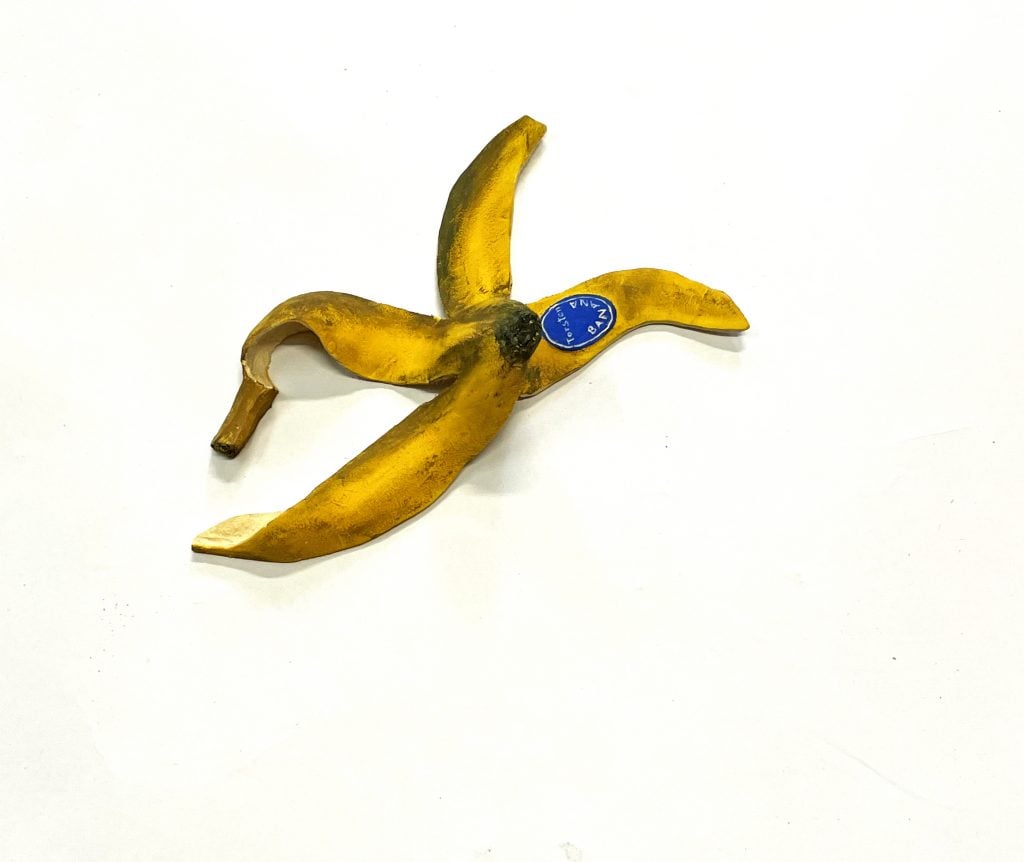 A small sculpture that looks exactly like a discarded banana peel with a blue label sticker reading Torstens Banana, part of the group exhibition 