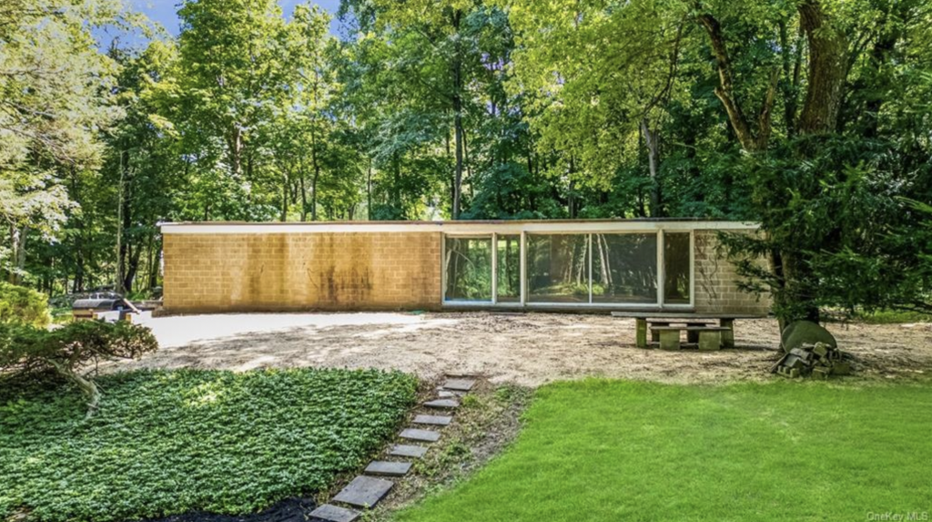 A photograph of the mid-century modern single story Booth House by Philip Johnson, situated amongst greenery with stone steps leading up to it.