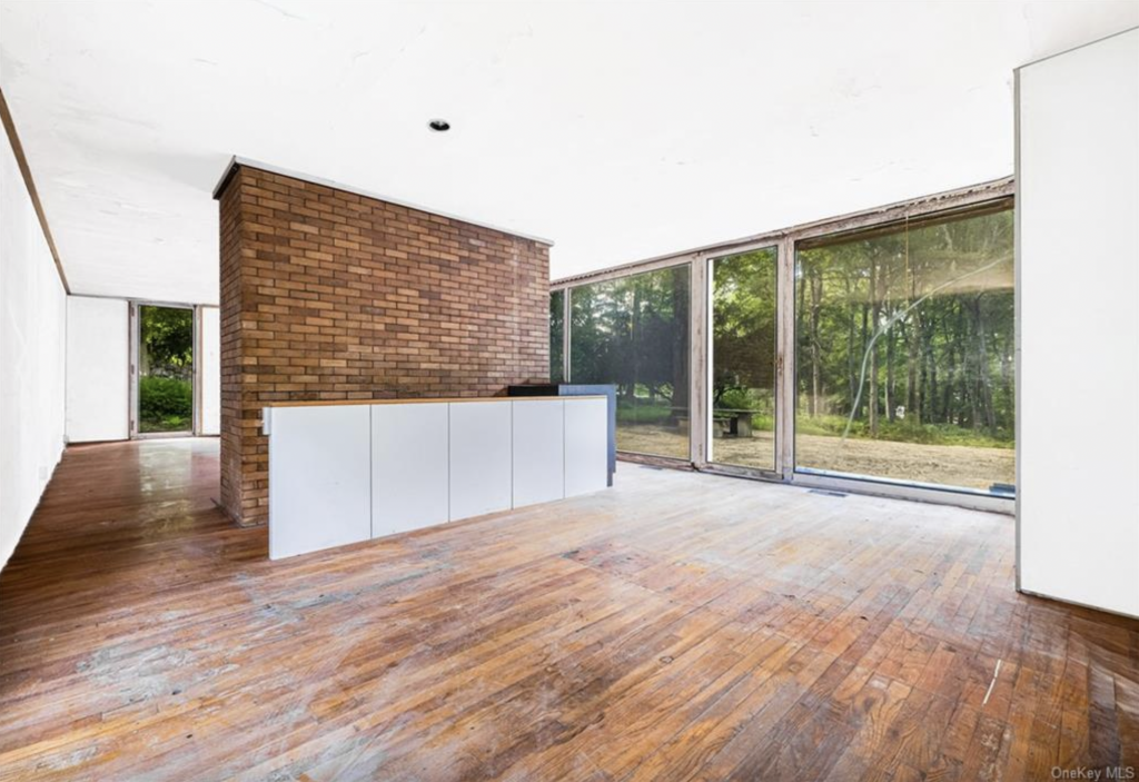 A photograph of the empty interior of the Philip Johnson Booth house, taken from behind its brick fireplace.