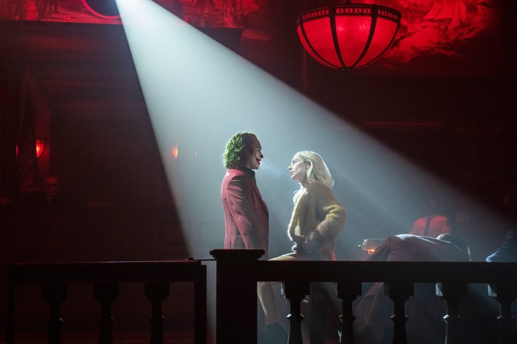 A spotlight shining on a man in green hair and clown makeup, and a blonde woman