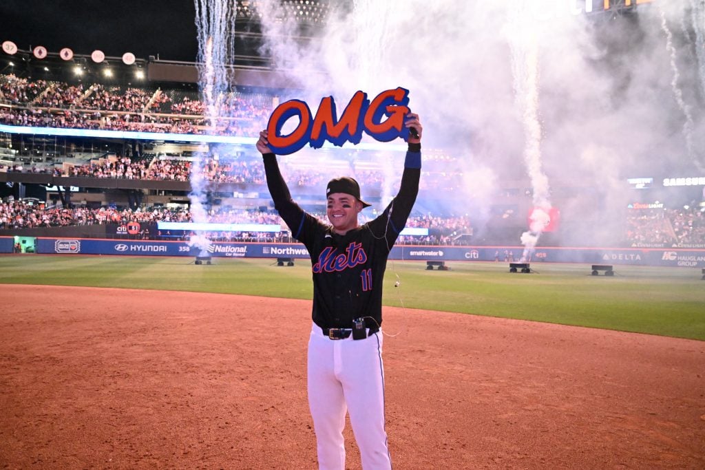 Infielder Jose Iglesias of New York Mets holds up a OMG sign by artist Jerome McCroy after the game against the Houston Astros at Citi Field on June 28, 2024. Iglesias gave a postgame concert to celebrate the release of his new single, also called "OMG." He is seen on the field in his black Mets jersey with white paints, in front of the white smoke from fireworks.