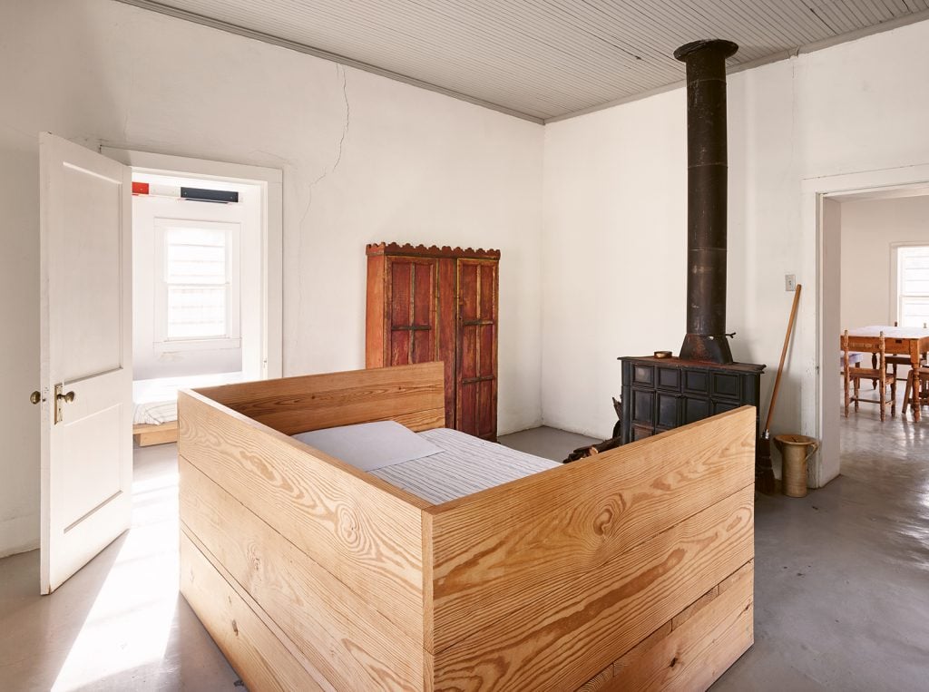 A photograph of a minimalist wooden day bed in a white room at the Marfa home of Donald Judd