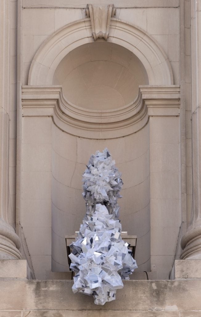 A photograph of a geometric, loosely abstract white sculpture in a facade niche on the exterior of the Met.