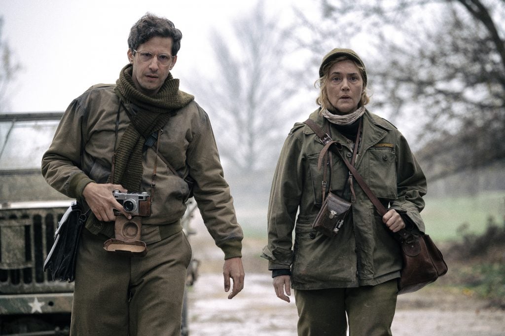 A man and woman wearing combat gear and armed with cameras walking away from a jeep