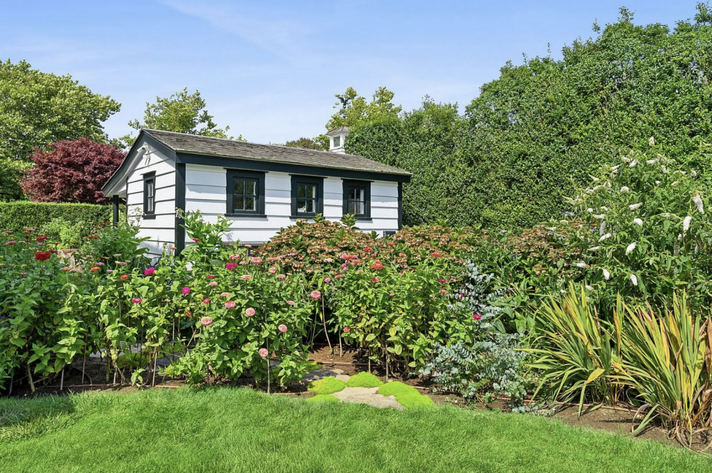 A photograph of a white and black clapboard building that once served as the studio of Roy Lichtenstein, surrounded by green grounds and flower gardens