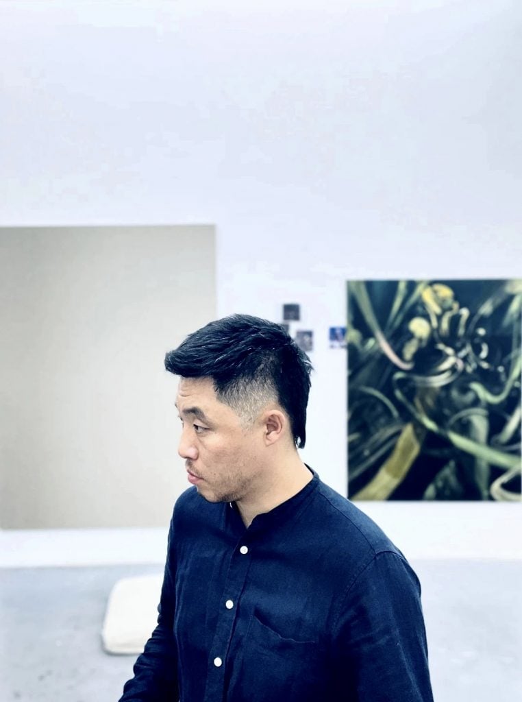 Side-profile portrait of the artist liu jian in his studio wearing a dark blue button down shirt.