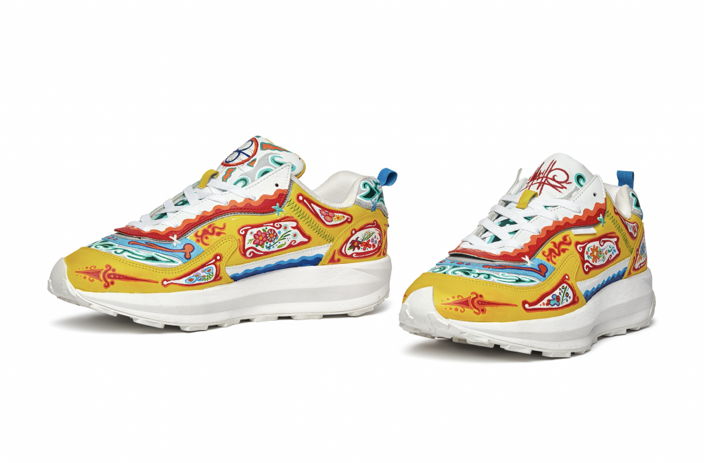 A photo of a pair of sneakers decorated with a bright floral pattern in hues of yellow, red, blue and green, both facing front and slightly to the left.