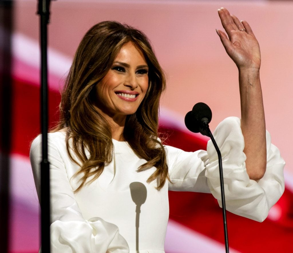 A woman, Melania Trump, waving from a podium